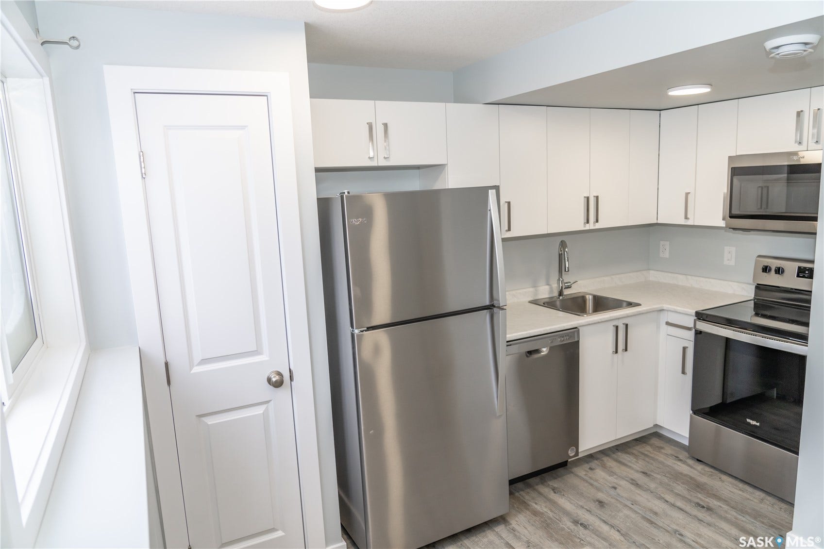 306 Stehwien Street, Saskatoon SK S7W 1P3 Kitchen featuring sink, appliances, light wood-type flooring, and white cabinetry