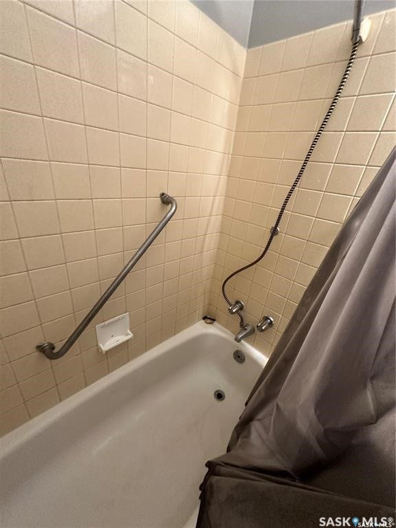 Built-in bathtub with a tile surround, wall-mounted grab bar, and a handheld shower fixture