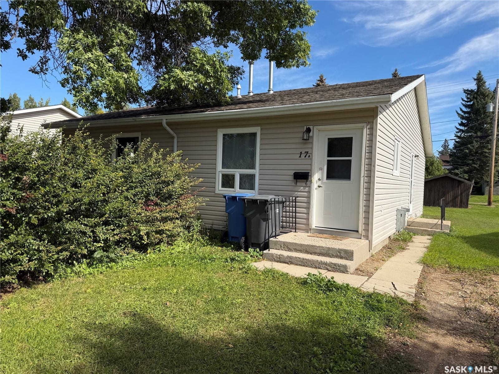 Cream-colored siding exterior with white trim, featuring a white entry door with a window panel, and a concrete stoop with two steps