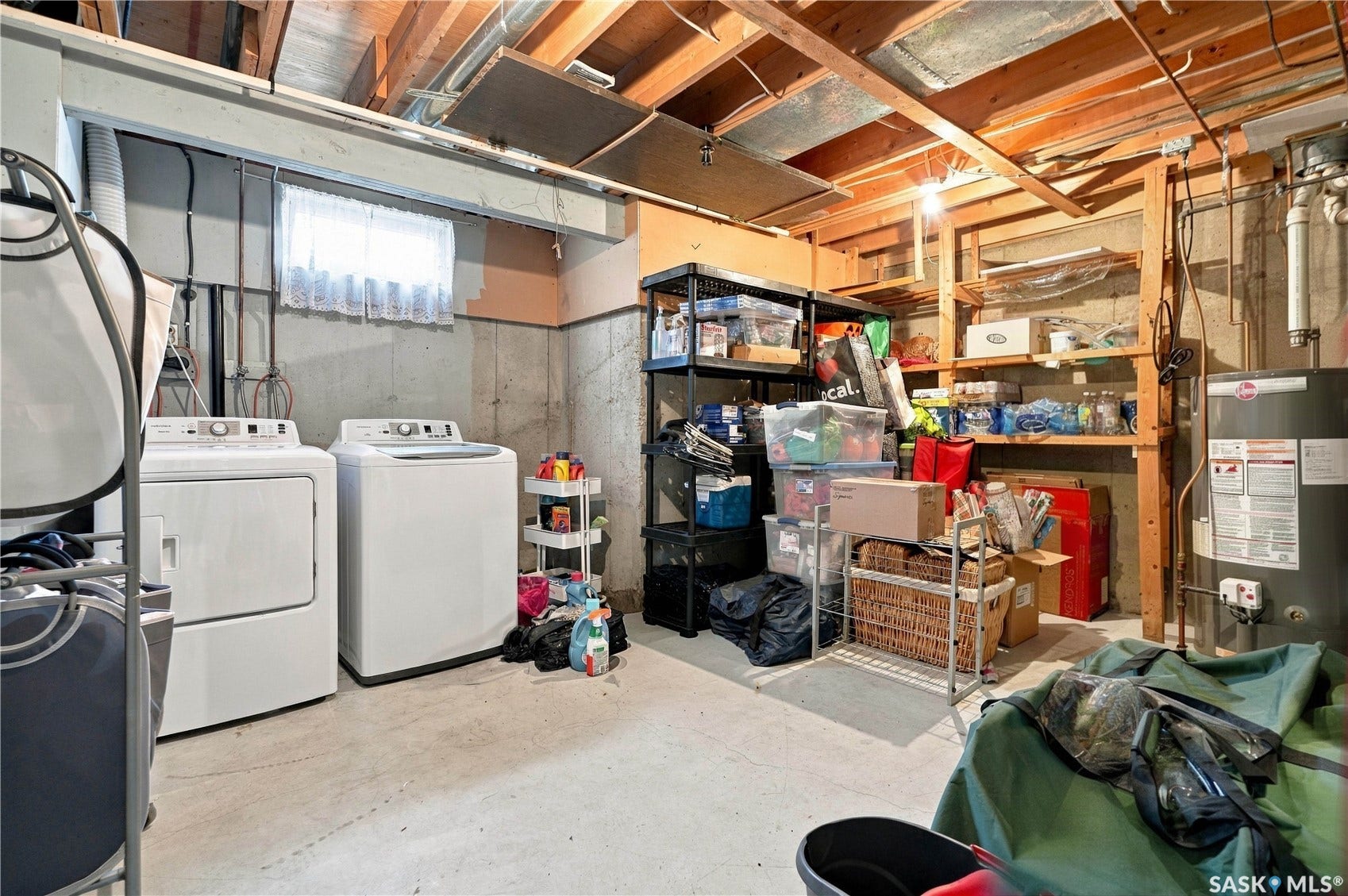 Laundry area with concrete flooring, exposed ceiling joists, built-in shelving, and a hot water heater