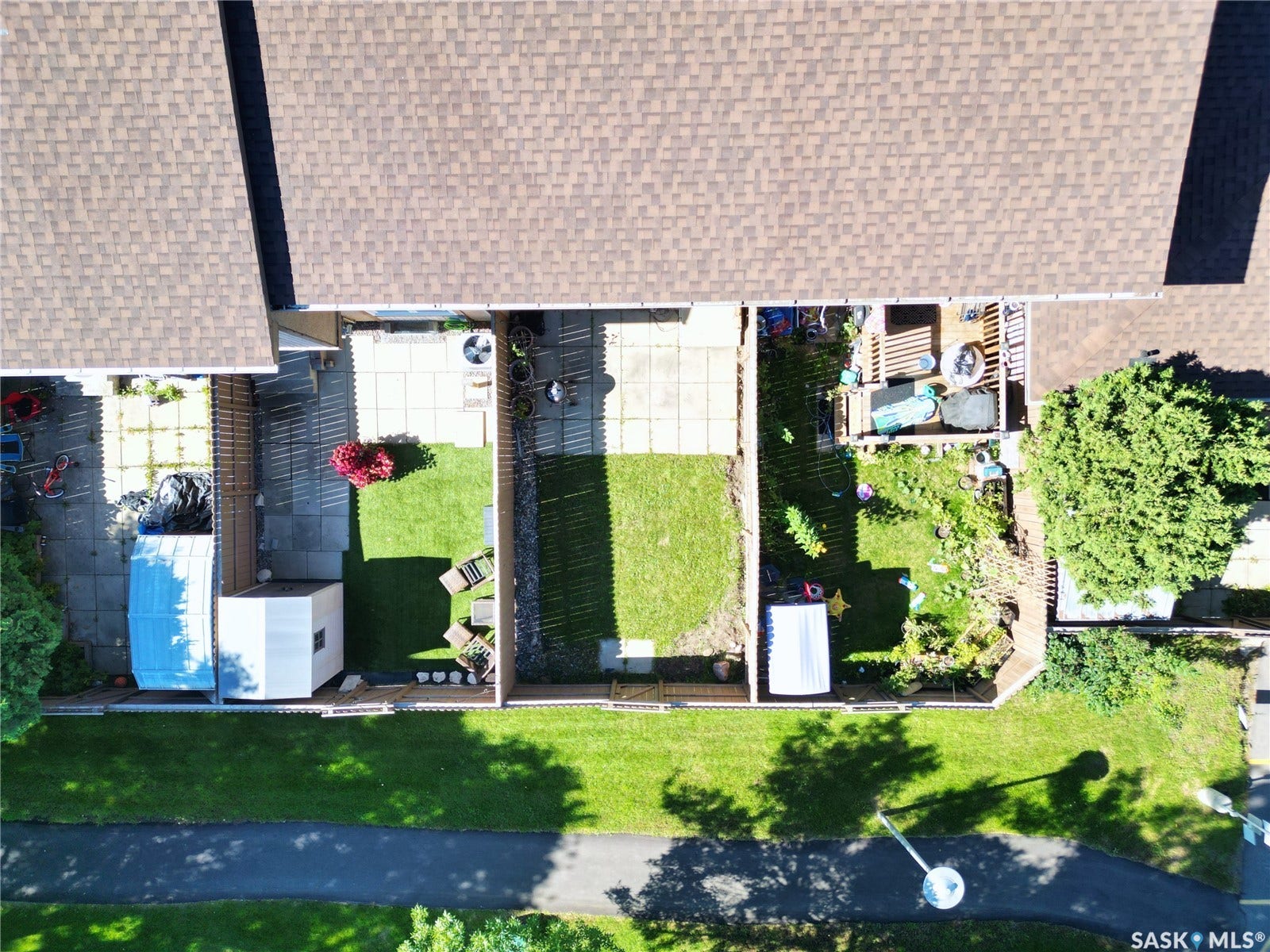 Individual patios, mature trees, manicured lawns, paved path, and brown shingle roofing