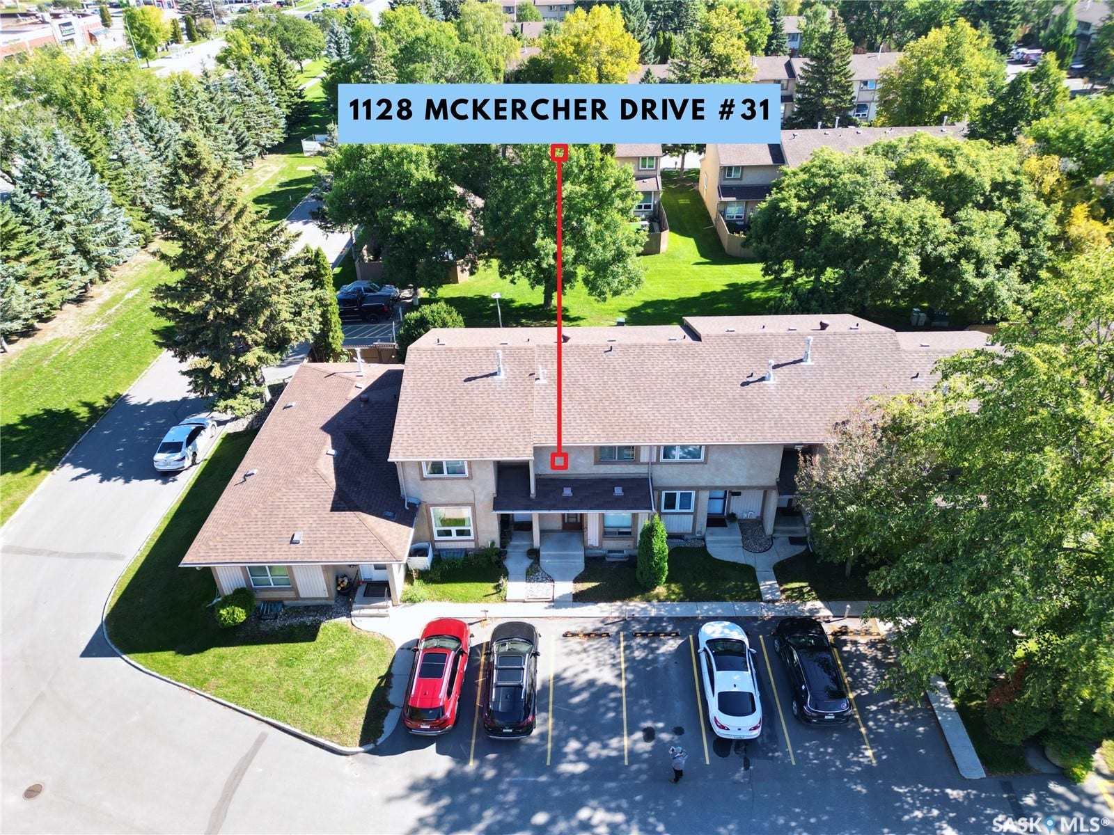Townhome property featuring a communal parking area, individual entrances, and surrounding green spaces with mature trees