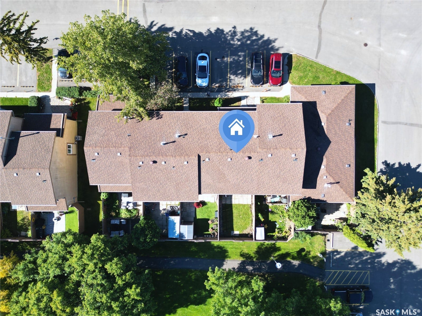Residential property featuring shingle roofing, paved parking areas, surrounding green spaces, and mature trees