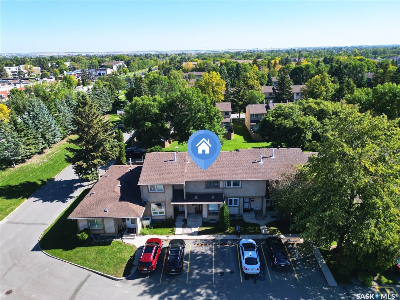 Multifamily residence with a brown shingle roof, ample surface parking, paved driveways, and surrounding green spaces