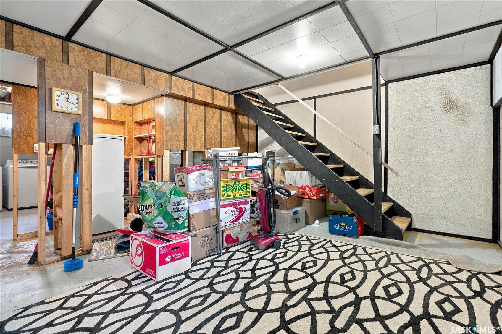 Finished basement area featuring wood-paneled walls, exposed ceiling grid, and a utility sink