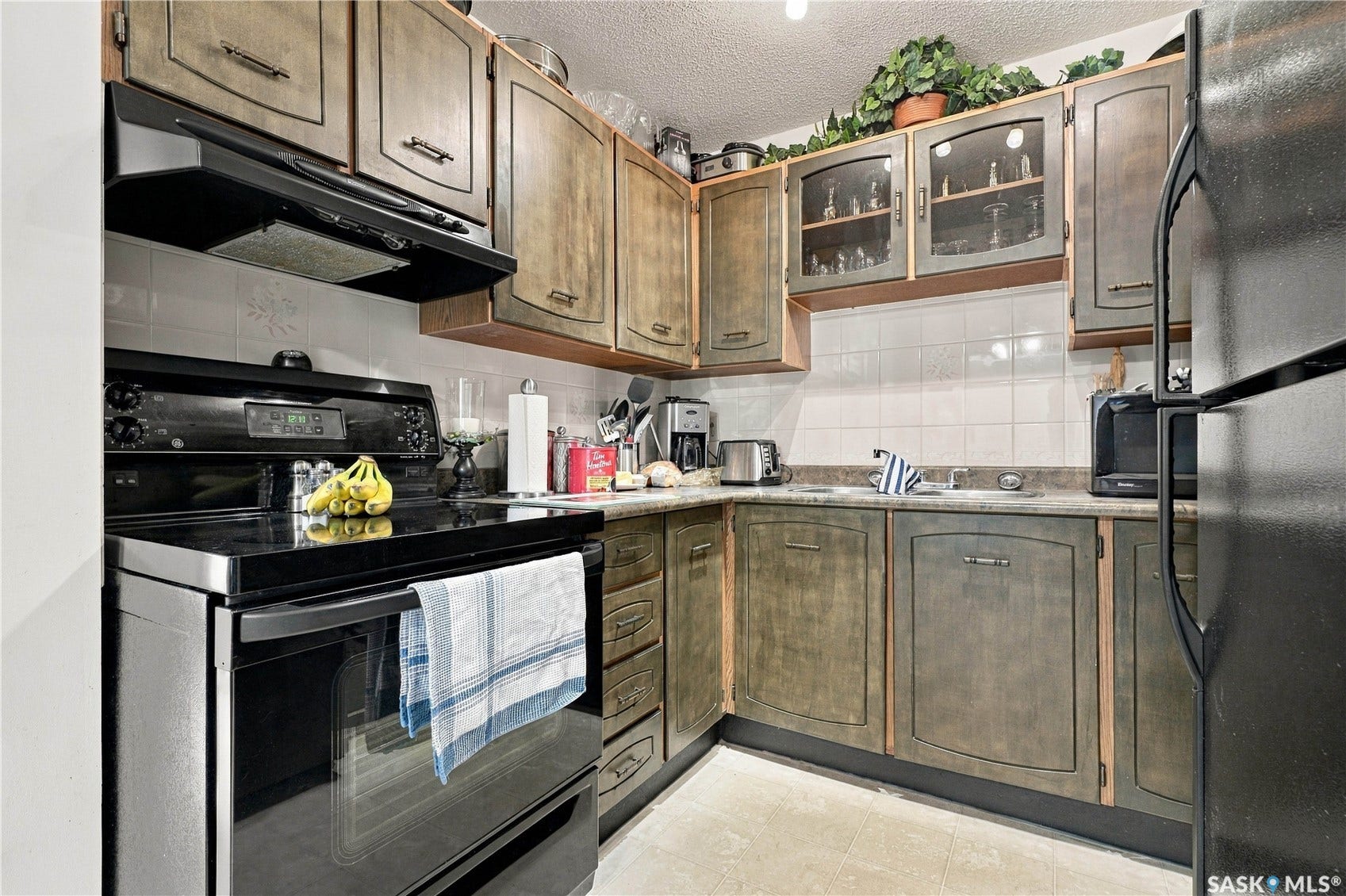 Kitchen featuring extensive cabinetry with varied door styles, ceramic tile backsplash, built-in range hood, and a dual-basin sink