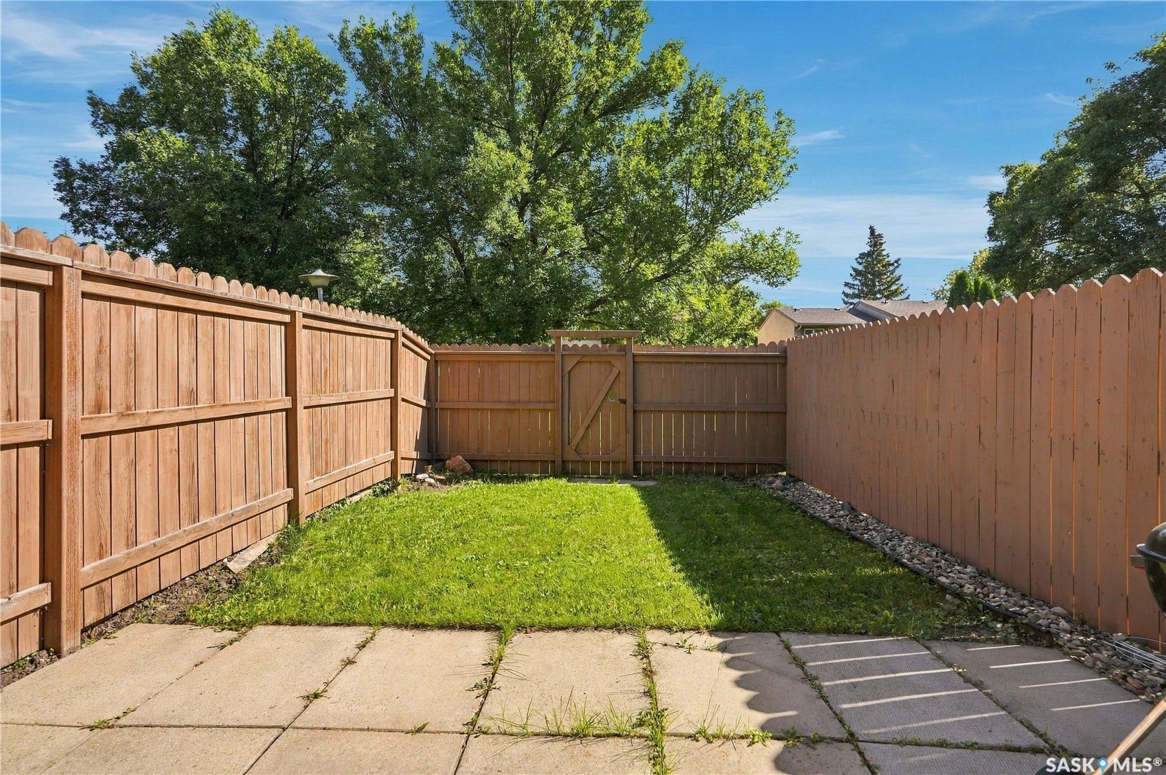 Paved patio area, natural wood fencing, a grass lawn, and a gate