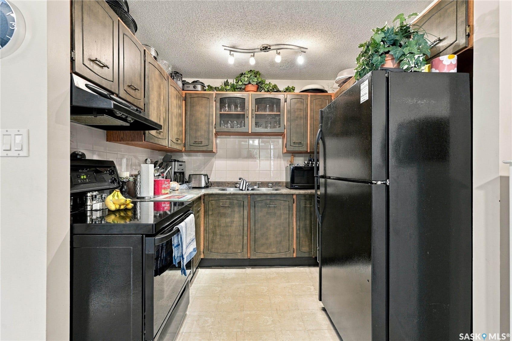 Kitchen featuring wood-finish cabinetry, black appliances, track lighting, and a tile backsplash