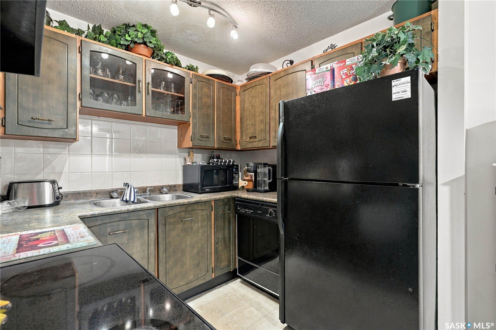 Kitchen featuring wood-finish cabinetry, white tiled backsplash, track lighting, and a dual-basin sink