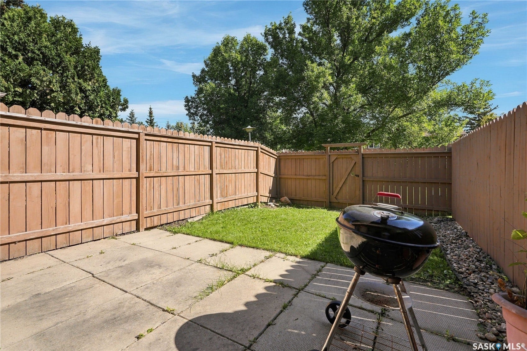 Fenced backyard with concrete patio, grass area, and a privacy gate