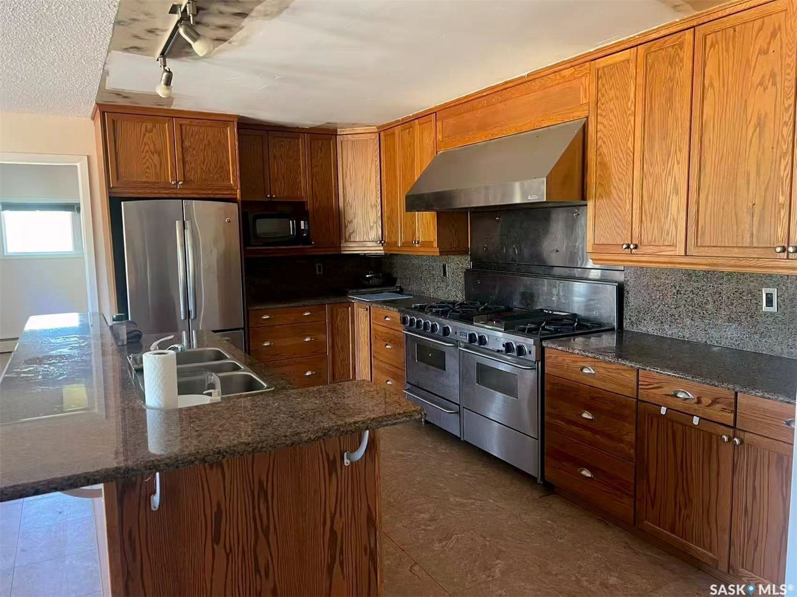 Kitchen featuring wood cabinetry, stainless steel appliances, a gas range with an oversized hood, and a dual basin sink with an extended countertop