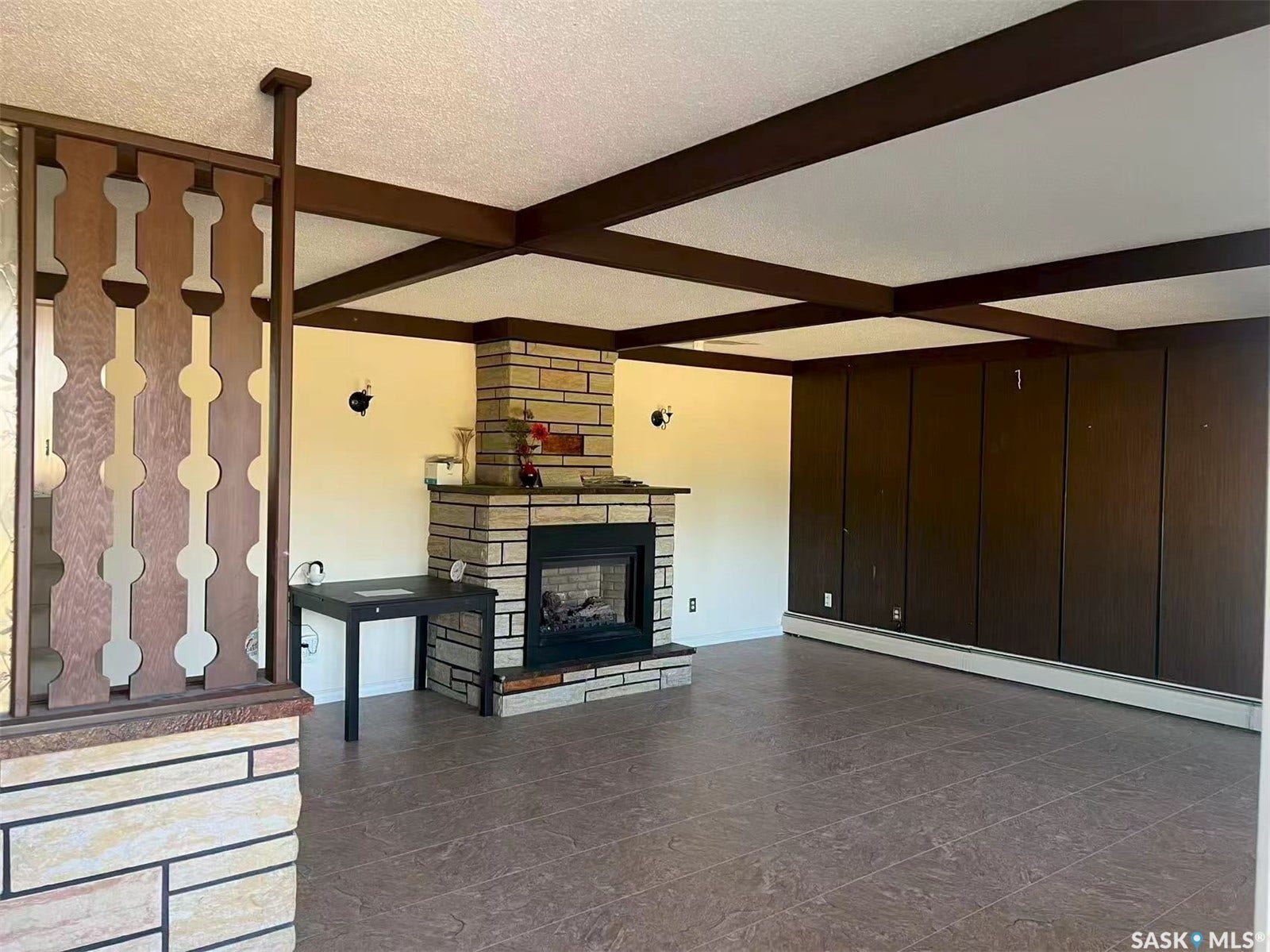 Exposed ceiling beams, full-height stone fireplace with hearth, built-in wall paneling, and tiled flooring
