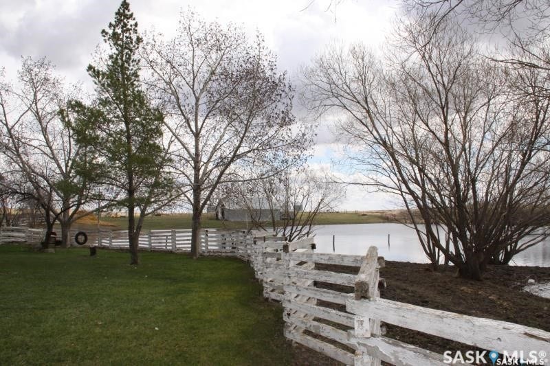 Expansive green lawn, white ranch-style fencing, mature deciduous trees, evergreen trees, and a body of water