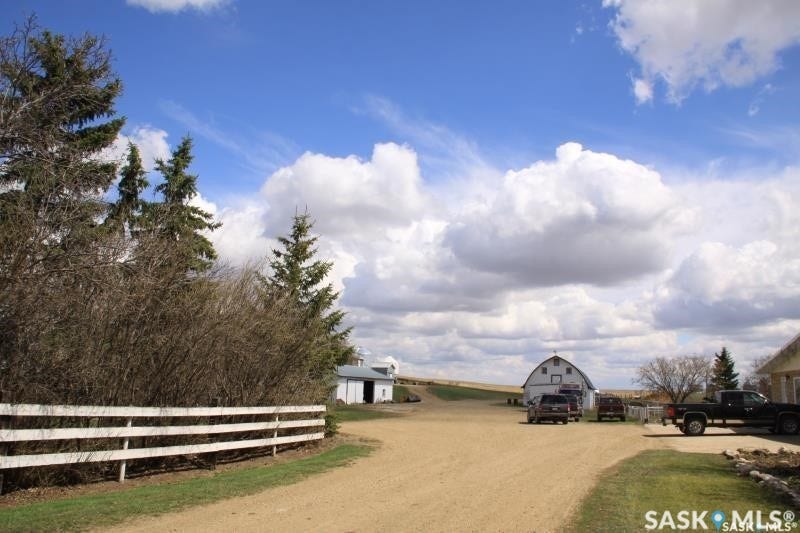 White three-rail fence bordering a gravel driveway, leading to a barn structure
