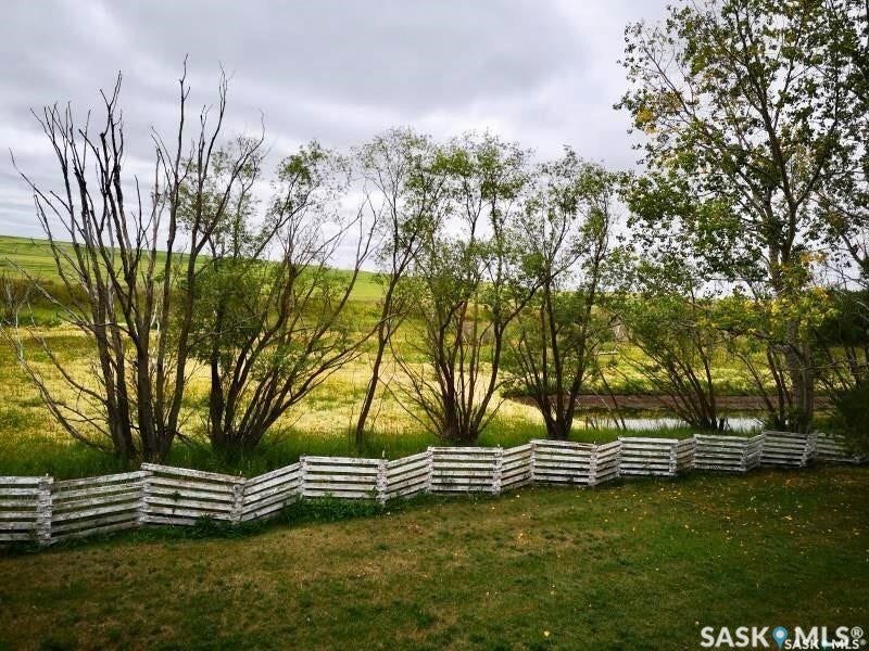 Expansive green lawn with a white wooden fence, mature trees, and a distant body of water