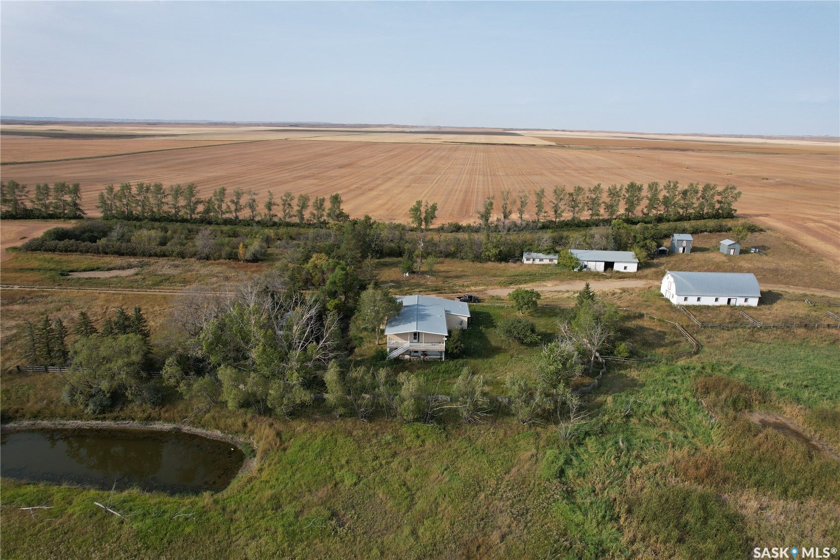 Expansive property featuring a residence, multiple outbuildings, a pond, mature trees, and surrounding agricultural land