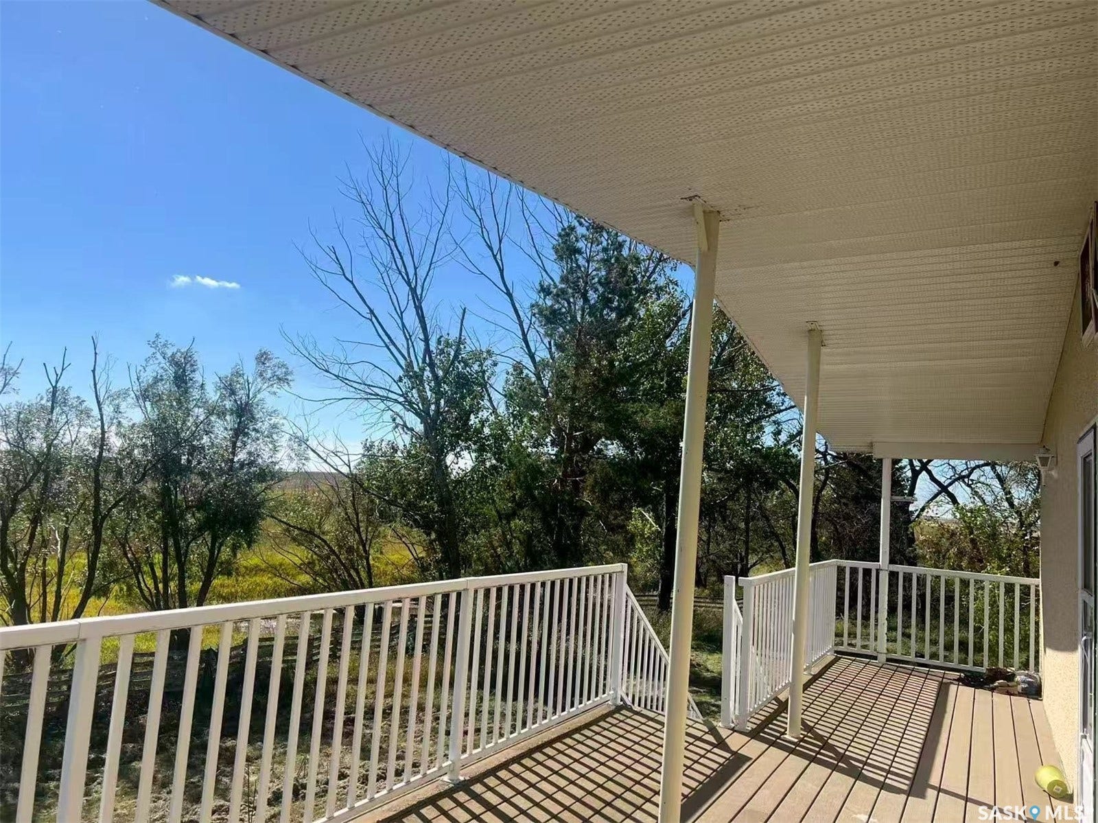 Covered porch featuring wood-finish decking, white metal railings, and support columns