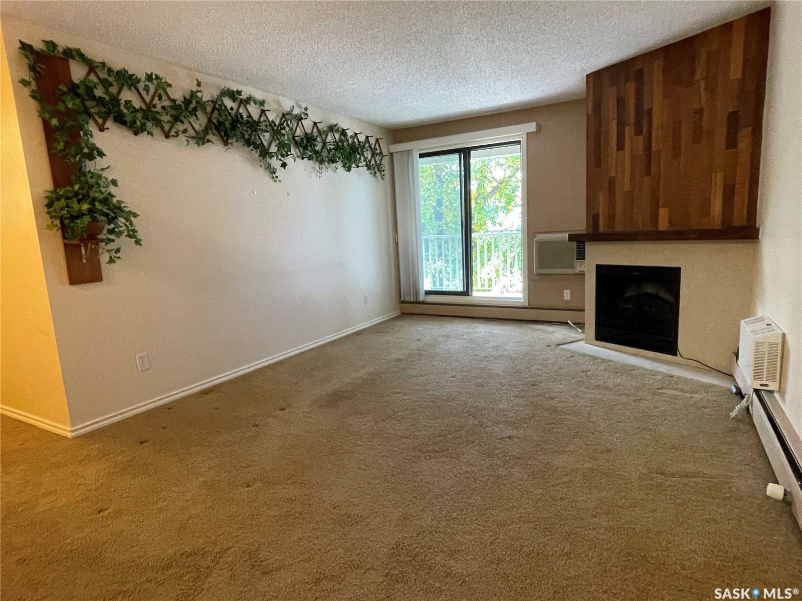 Carpeted living space with a built-in fireplace, wood-panel accent wall, and sliding glass door leading to a balcony