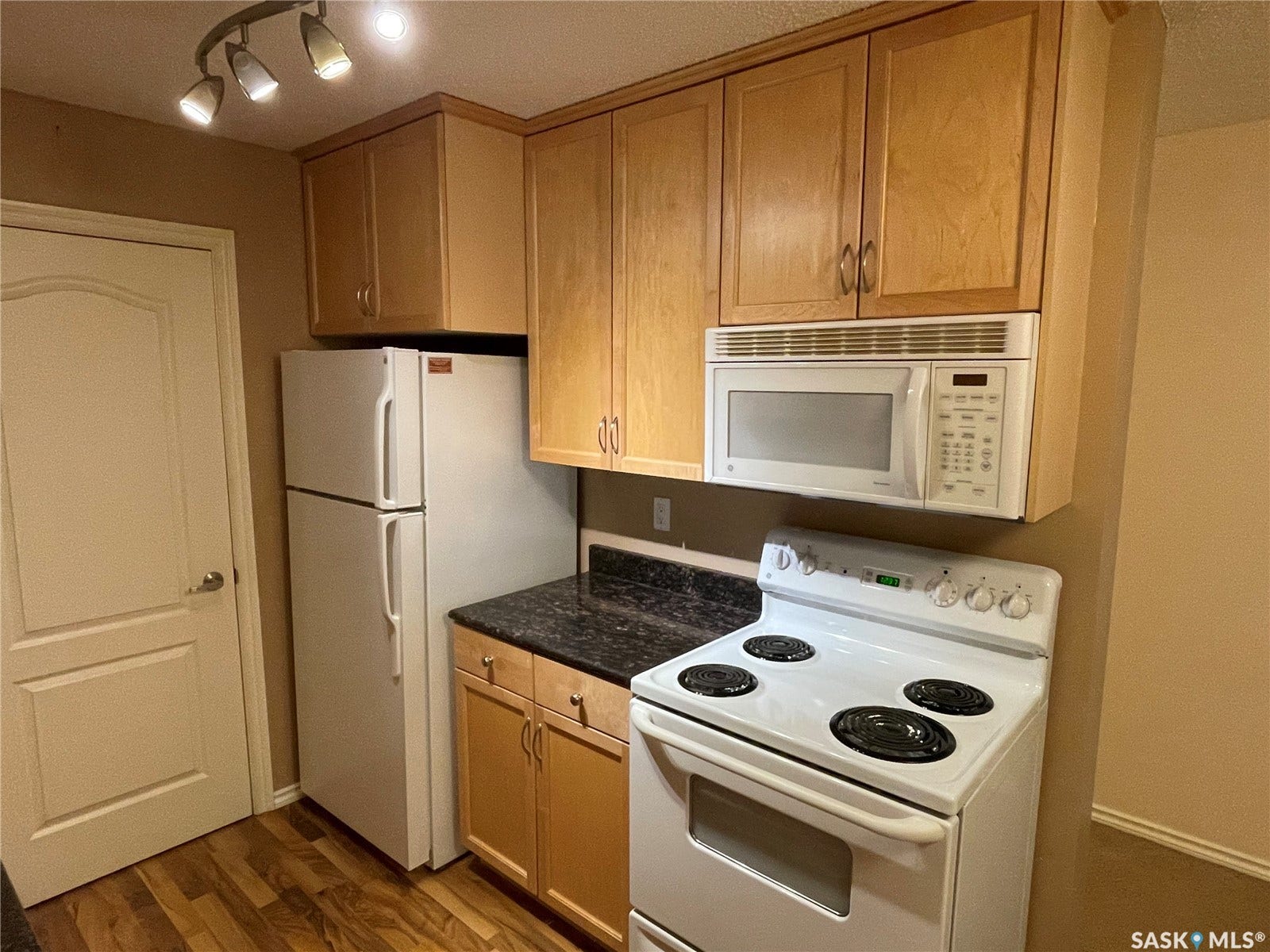 Kitchen featuring wood-finish cabinetry, black stone-finish countertops, and a full suite of white appliances including a refrigerator, electric range, and over-the-range microwave