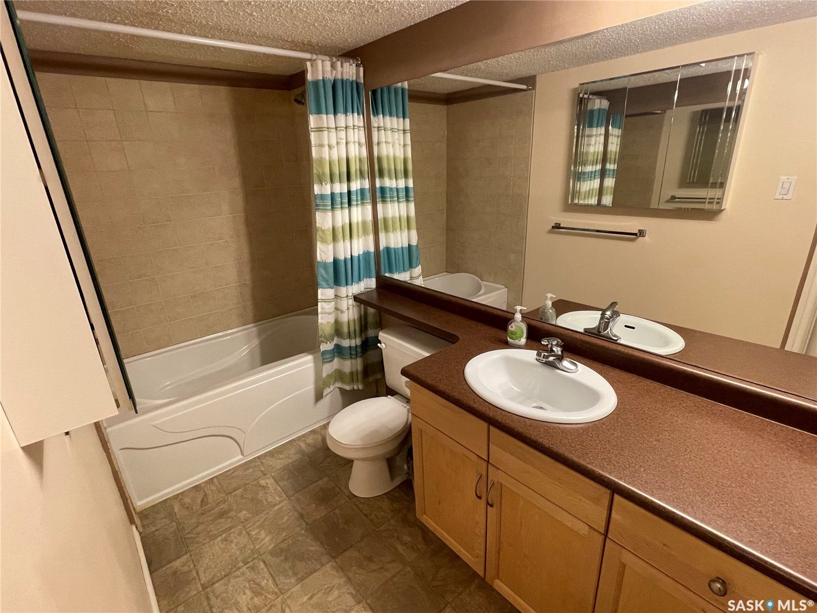 Double vanity with integrated sinks, wood-finish cabinetry, and a full-width mirror, tile tub surround and medicine cabinet.