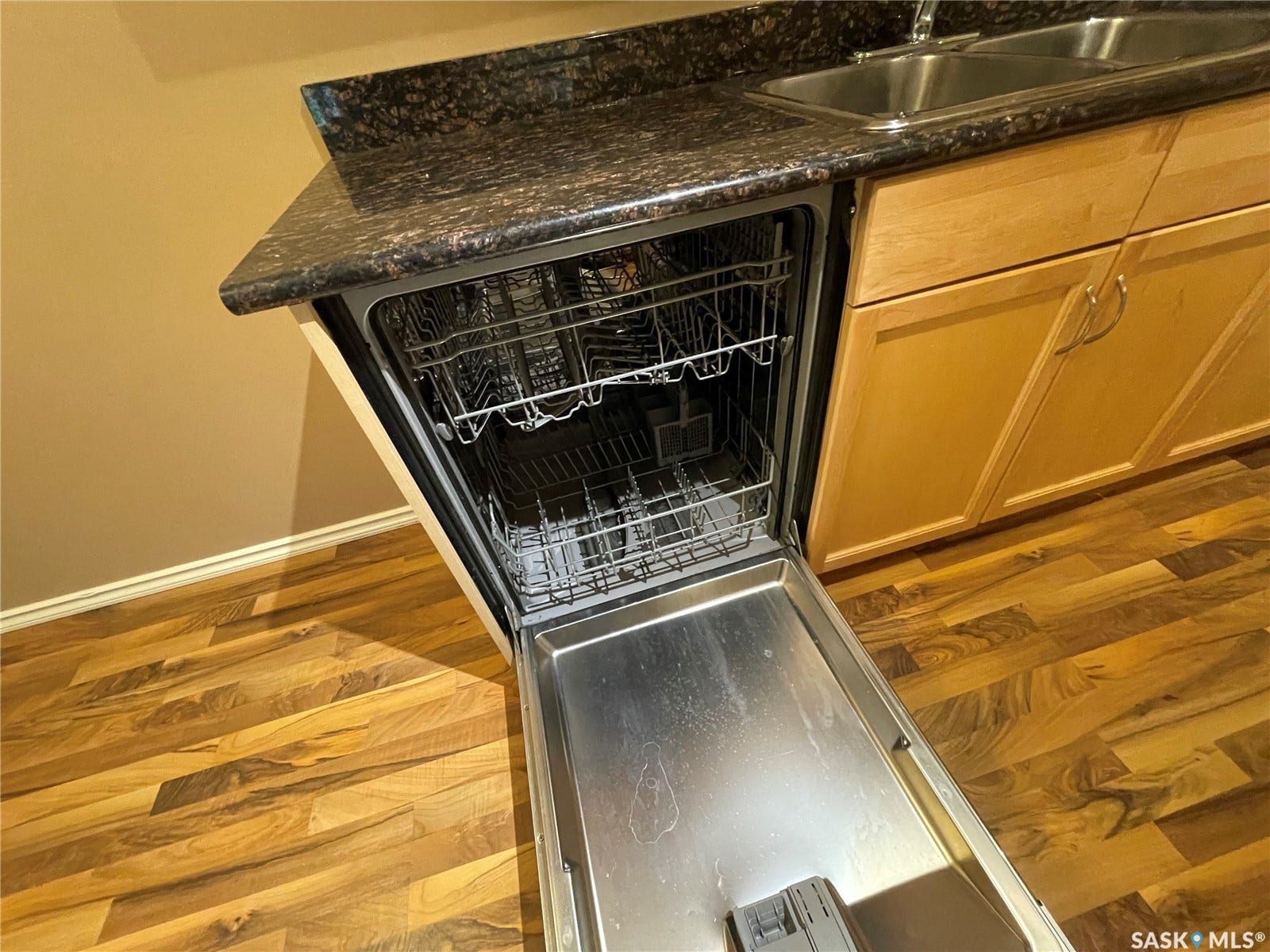 Wood-finish flooring, dark speckled countertop, light wood cabinetry, stainless steel double basin sink, integrated dishwasher