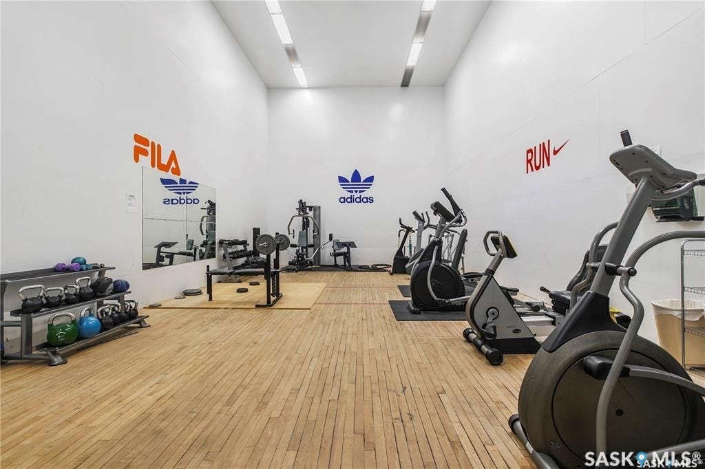 Spacious fitness area featuring wood flooring, mirrored wall, recessed lighting, and high ceilings