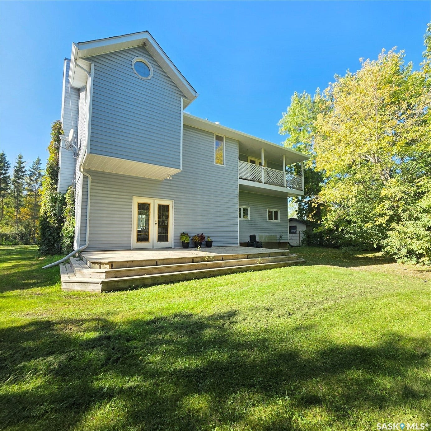 Multi-level deck with double French doors, large grassy area, and upper-level balcony with white railing