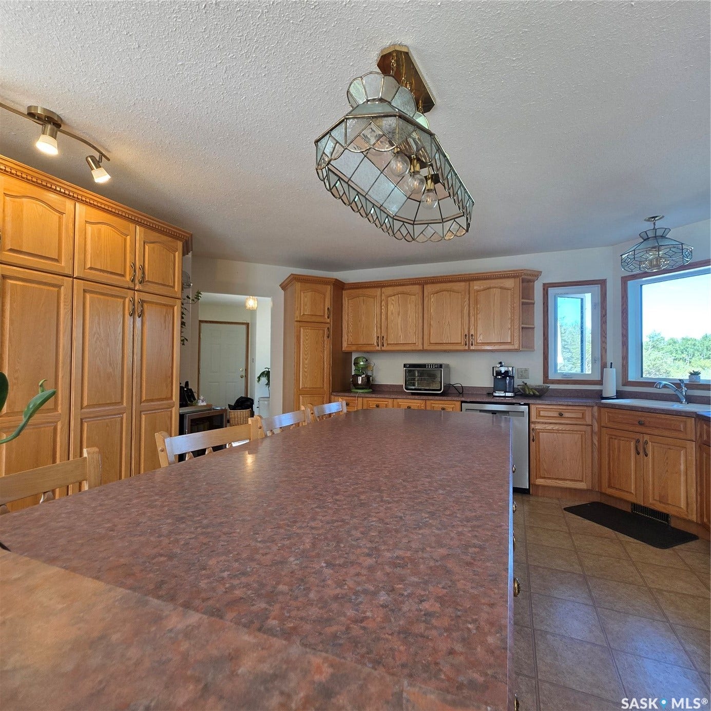 Kitchen featuring ample wood cabinetry, a large kitchen island with a patterned countertop, a built-in stainless steel dishwasher, and tile flooring