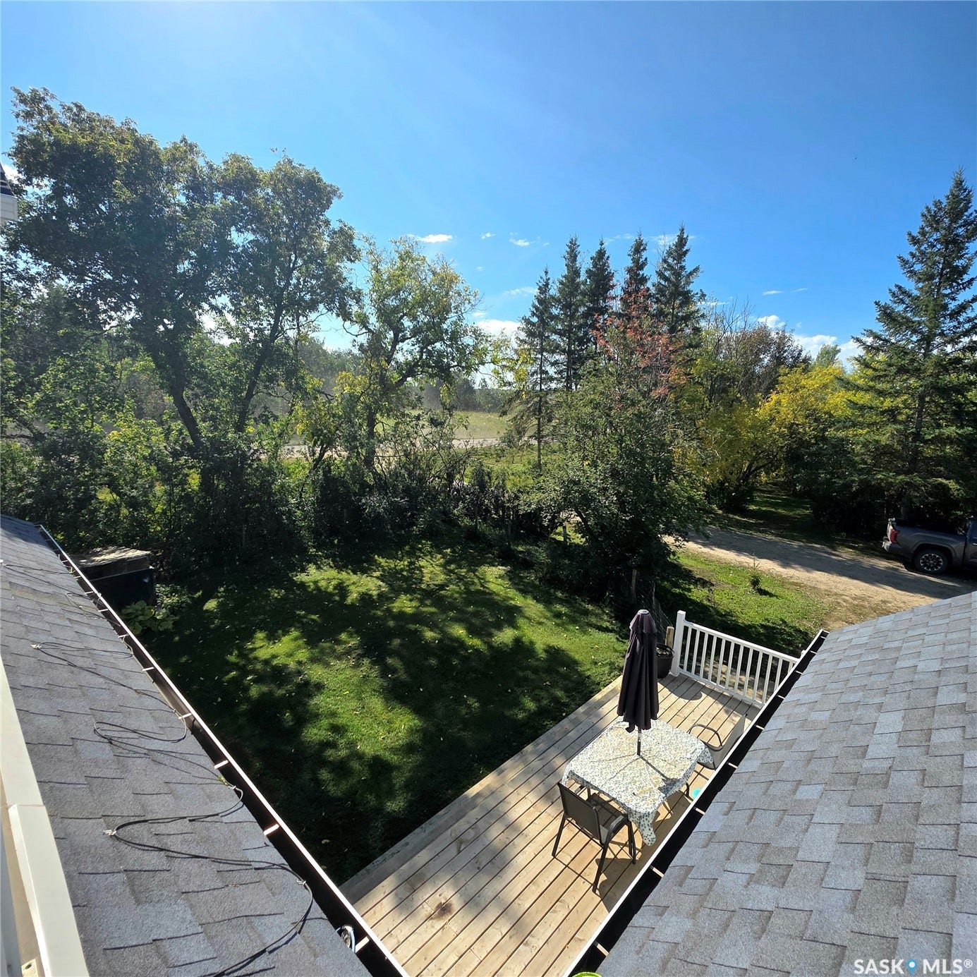 Expansive outdoor deck with white railing, overlooking a large lawn area and mature trees