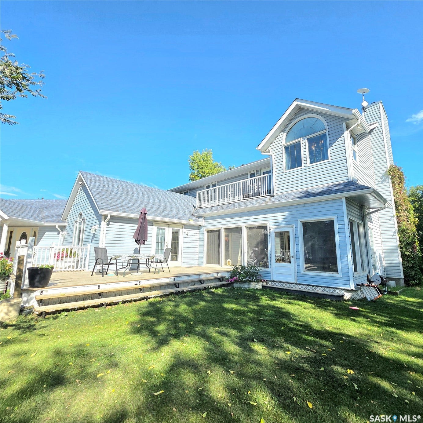 Expansive rear exterior with light blue siding, a multi-level wood deck, and a lower-level sunroom