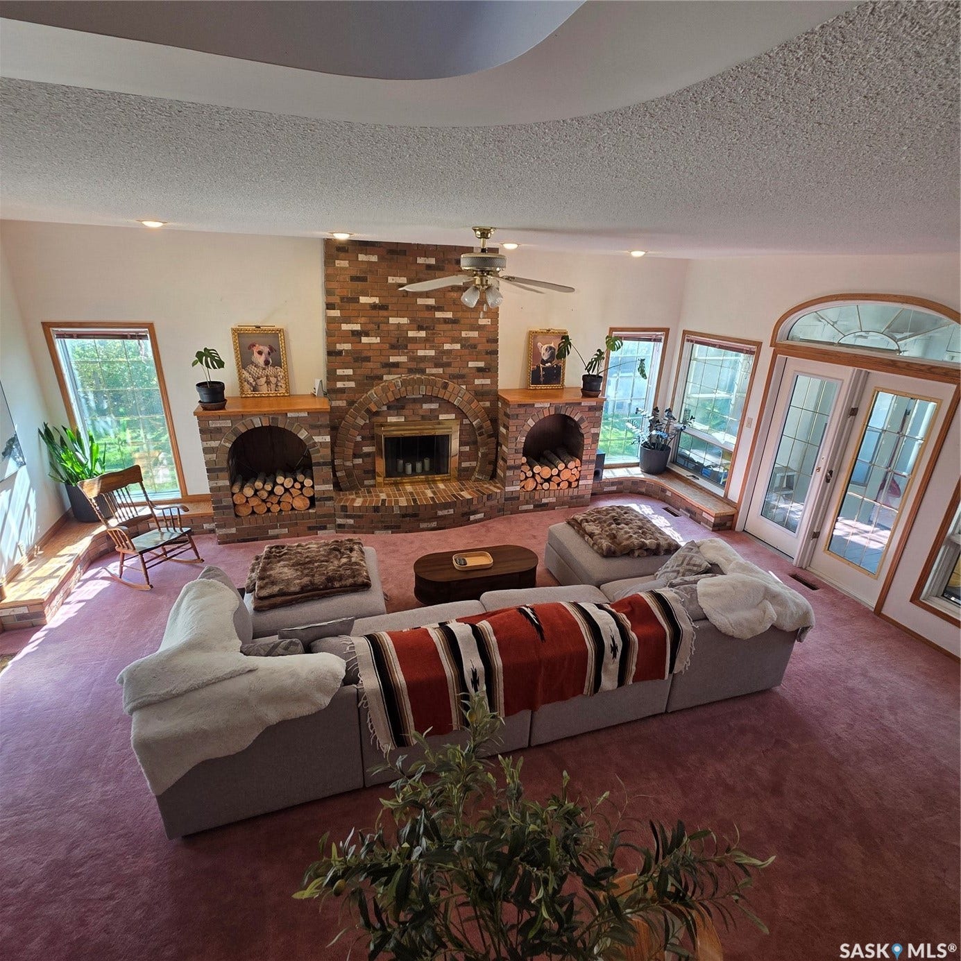 Expansive living area featuring a brick fireplace, arched windows, and French doors