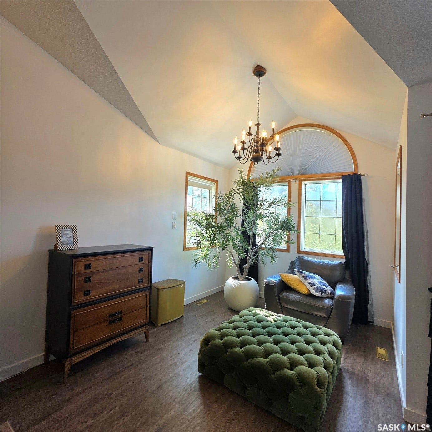 Vaulted ceiling with a chandelier, wood-finish flooring, and multiple windows including an arched window