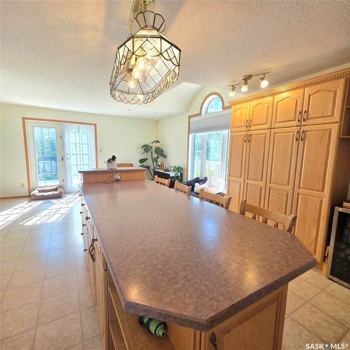 Expansive kitchen island with a durable countertop, extensive wood-finish cabinetry, arched window, and dual French doors