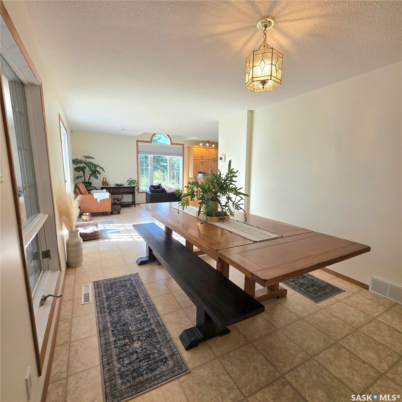 Tile flooring in an open-concept living area with an ornate ceiling light fixture, a window with an arched transom, and recessed lighting in the background