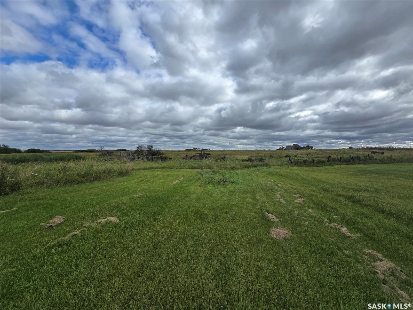 Expansive green acreage with distant structures under a vast sky