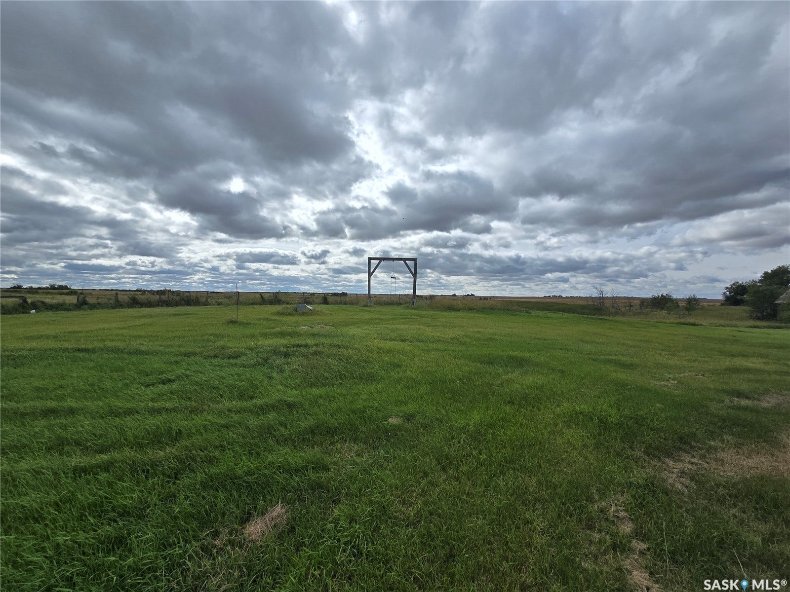 Expansive green space featuring a distant agricultural field, a dark-toned archway, and a wide-open sky