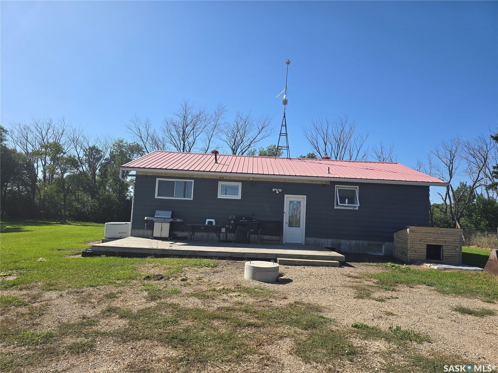 Rear exterior with a red metal roof, dark siding, and a concrete patio