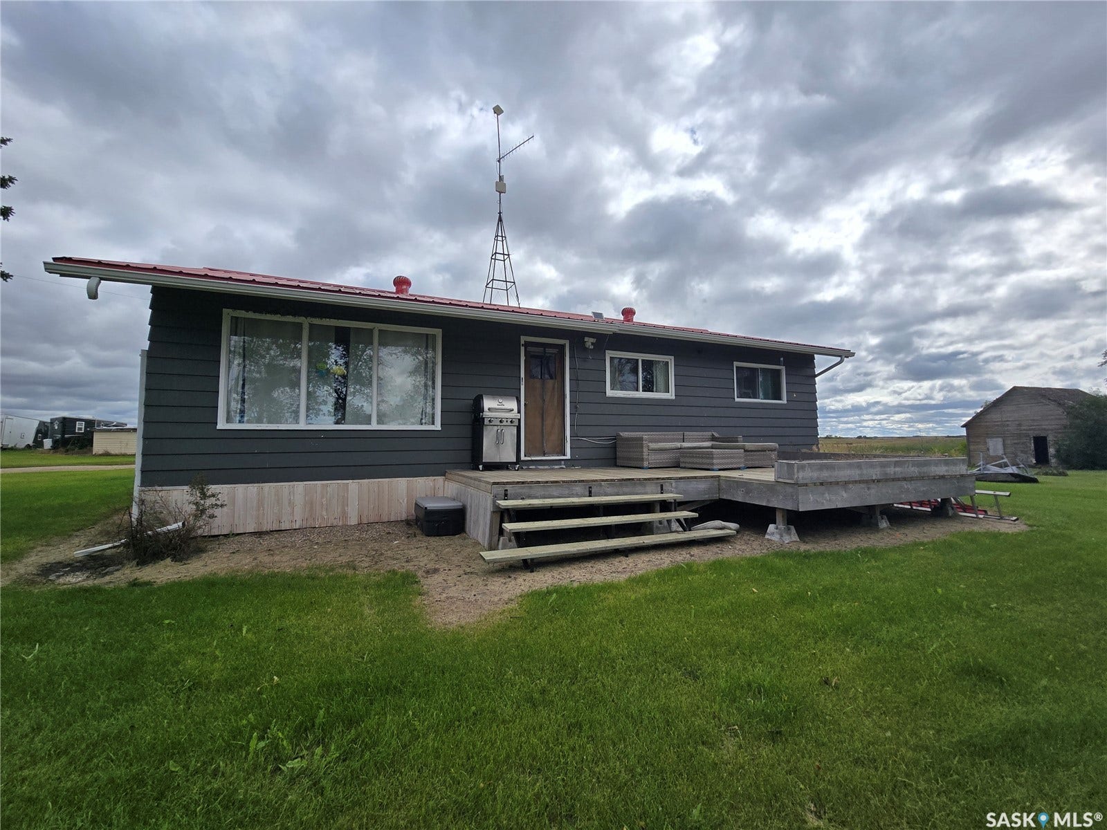 Exterior featuring dark gray horizontal siding, a red sloped roof, and an expansive wooden deck
