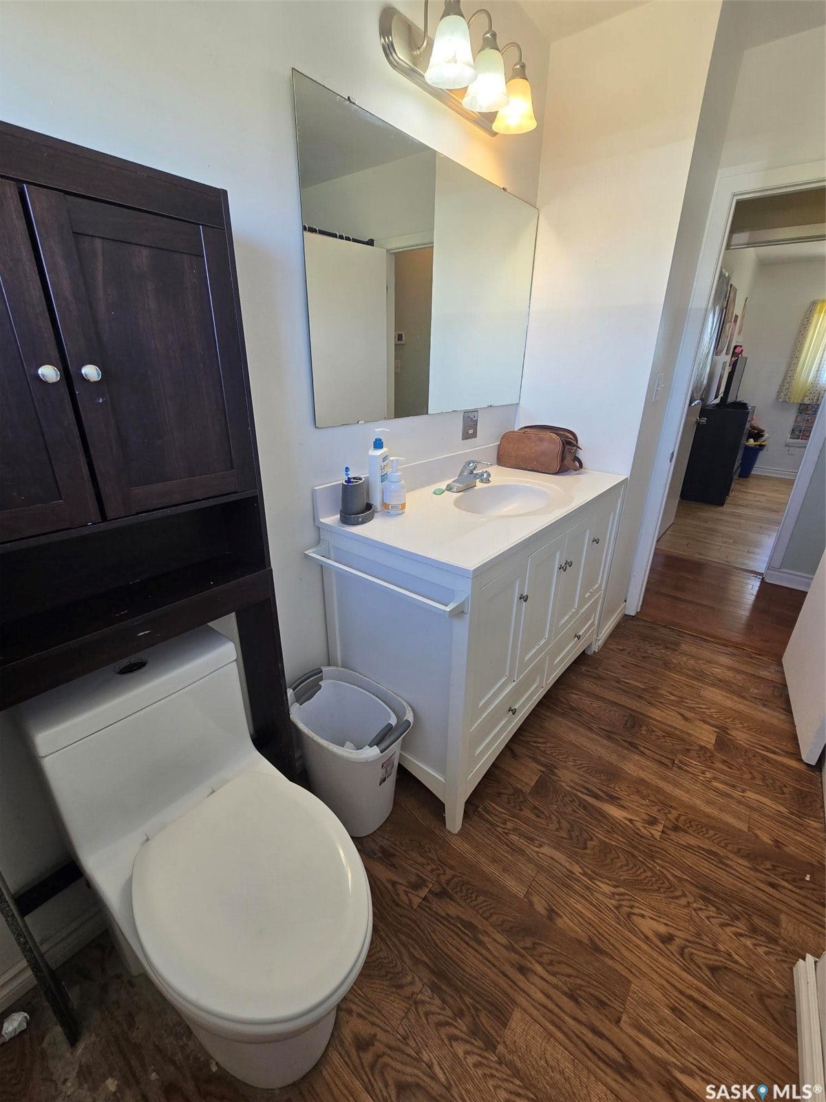 White vanity with an integrated sink, wall-mounted mirror, and wood-finish flooring