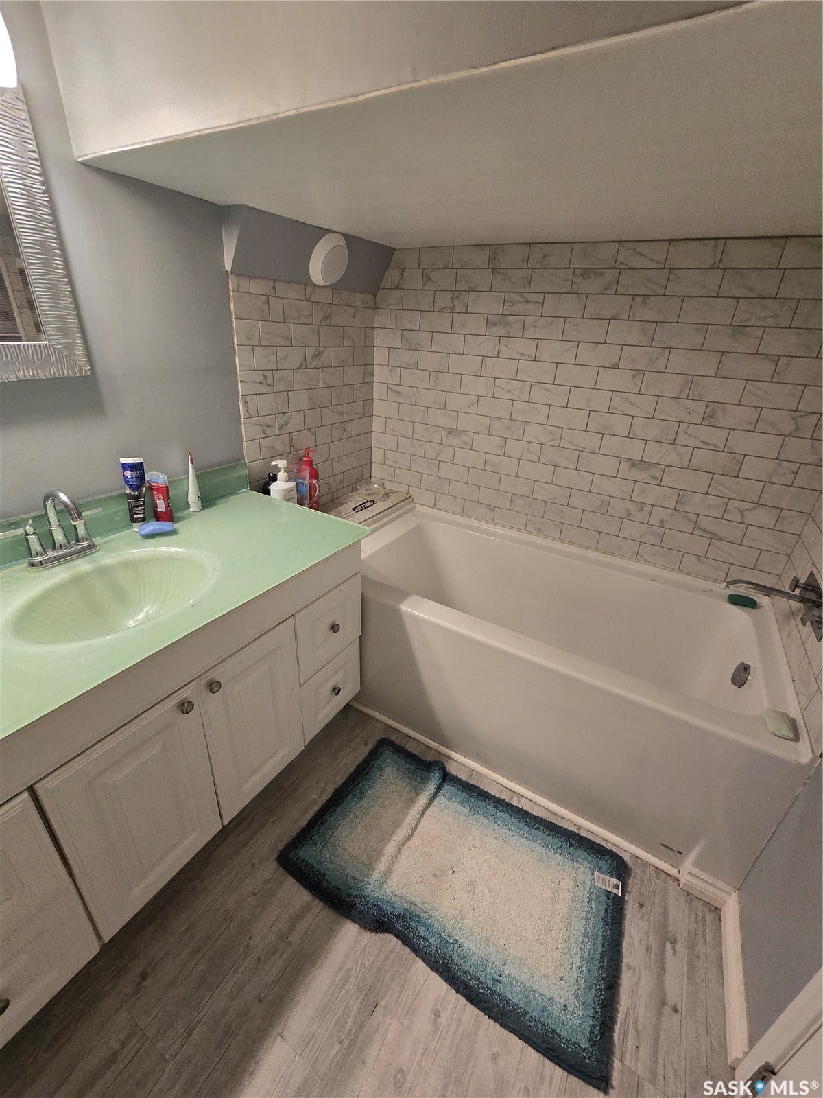 BASEMENT Bathtub with subway tile surround, vanity with integrated sink, white cabinetry, and wood-finish flooring