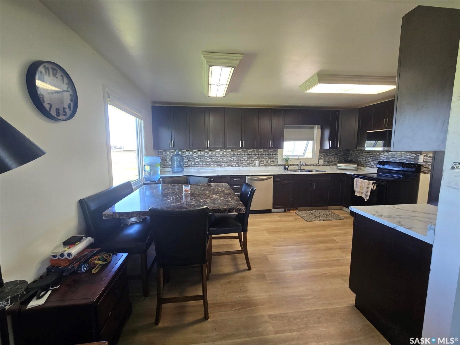 Kitchen featuring dark wood-finish cabinetry, mosaic tile backsplash, stainless steel dishwasher, built-in microwave, and wood-finish flooring