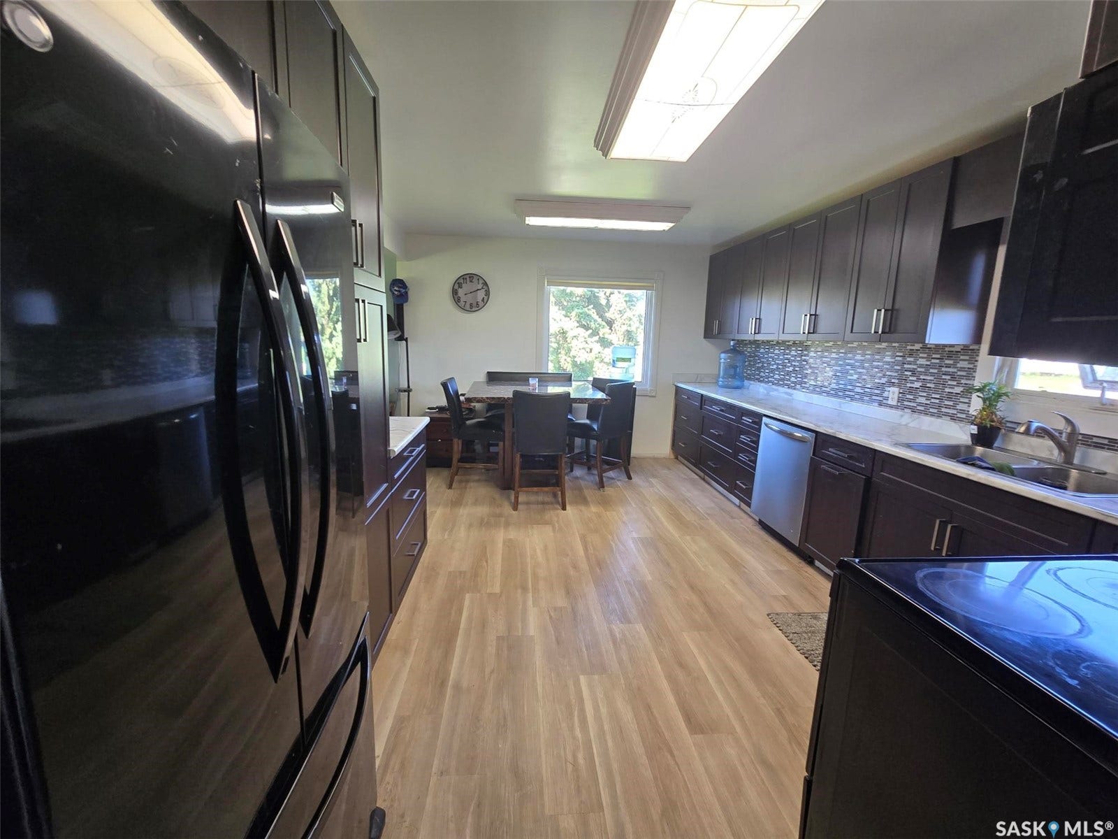 Expansive kitchen featuring wood-finish flooring, dark wood cabinetry, light-toned countertops, a mosaic tile backsplash, and stainless steel appliances