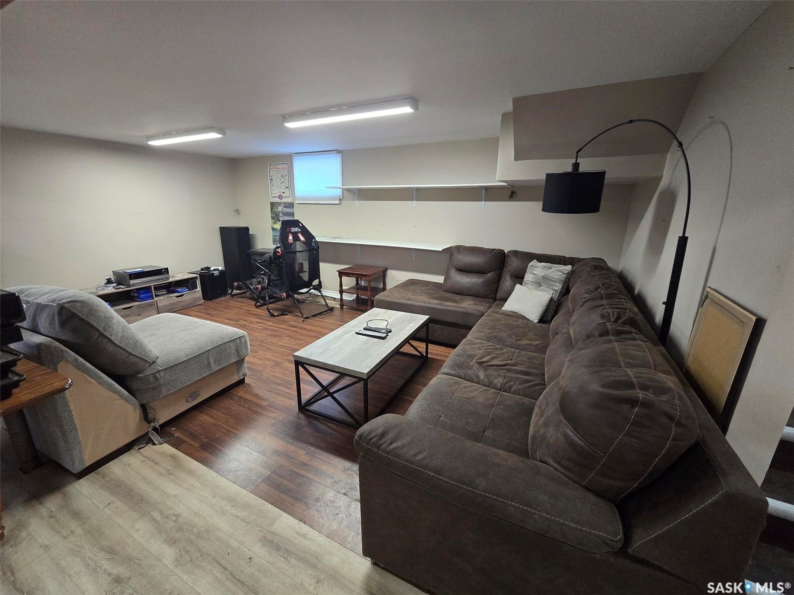Wood-finish flooring with a partial lighter wood-finish flooring section, built-in shelving, and a window with a roller shade