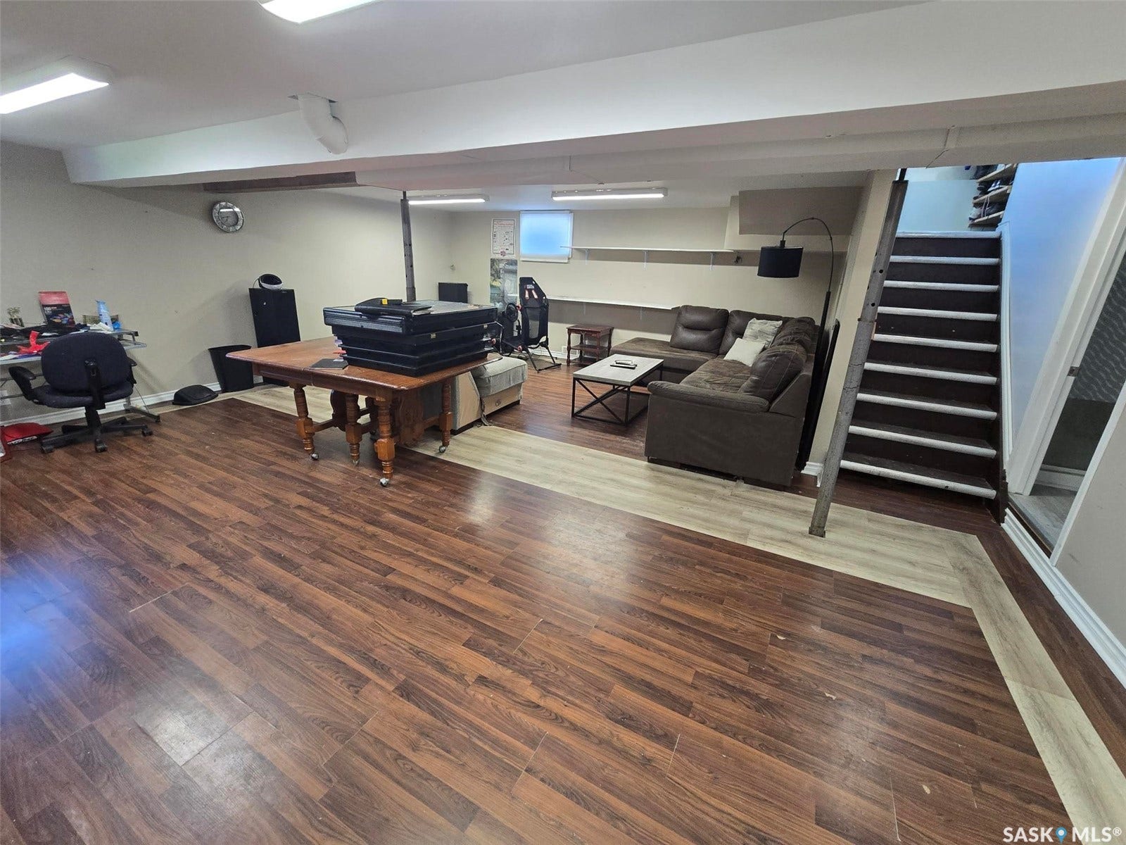 Expansive finished area with multi-tone wood-finish flooring, recessed lighting, and a built-in wall shelf