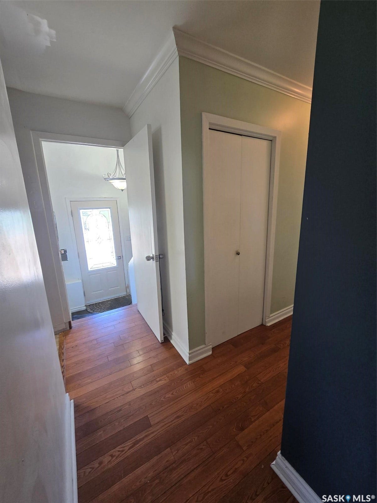 Hardwood-finish flooring, white bi-fold closet doors, crown molding, and a partial decorative glass entry door