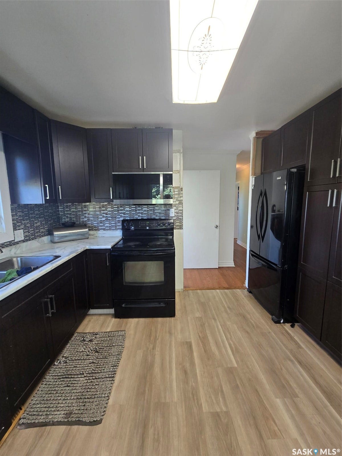 Kitchen featuring wood-finish flooring, dark cabinetry, white countertops, and a tiled backsplash