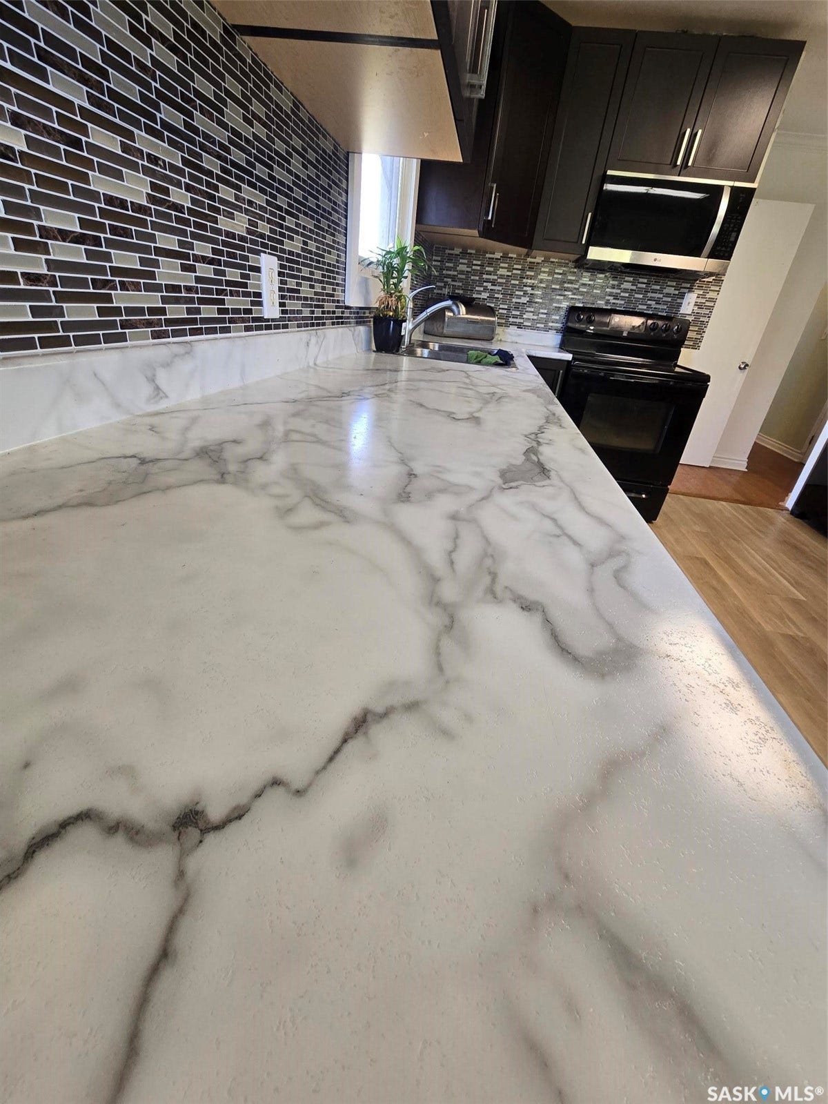 White veined countertops, dark wood-finish cabinetry, mosaic tile backsplash, stainless steel sink, and black appliances