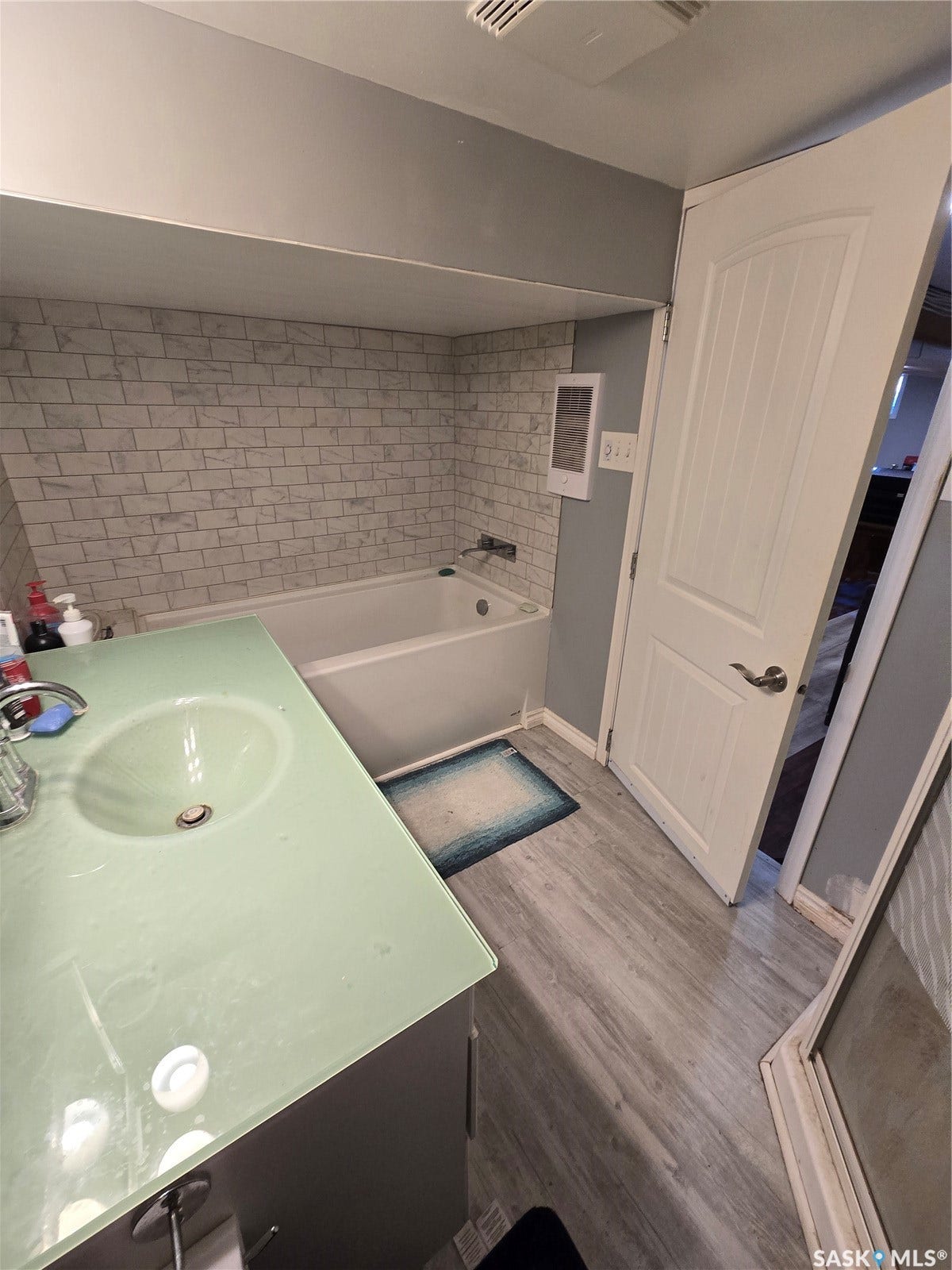 BASEMENT Bathroom featuring a built-in bathtub with subway tile surround, wood-finish flooring, and a vanity with an integrated basin sink
