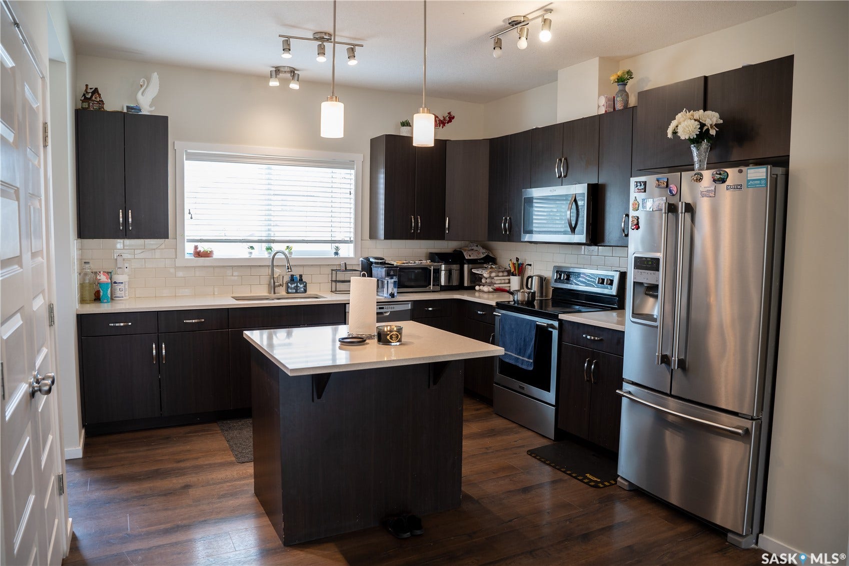 Kitchen featuring dark wood-finish cabinetry, stainless steel appliances, a white subway tile backsplash, and a central island with a white countertop