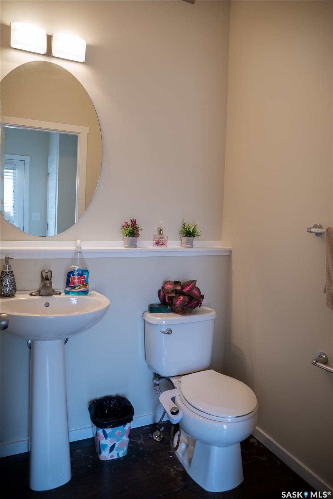 Pedestal sink with chrome faucet, circular mirror, and wall-mounted light fixture